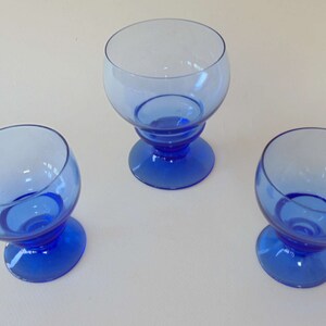 Op de afbeelding: Drie blauwe glazen bekers met een ronde kom en een korte steel. De bekers zijn gemaakt van helder glas met een blauwe tint.