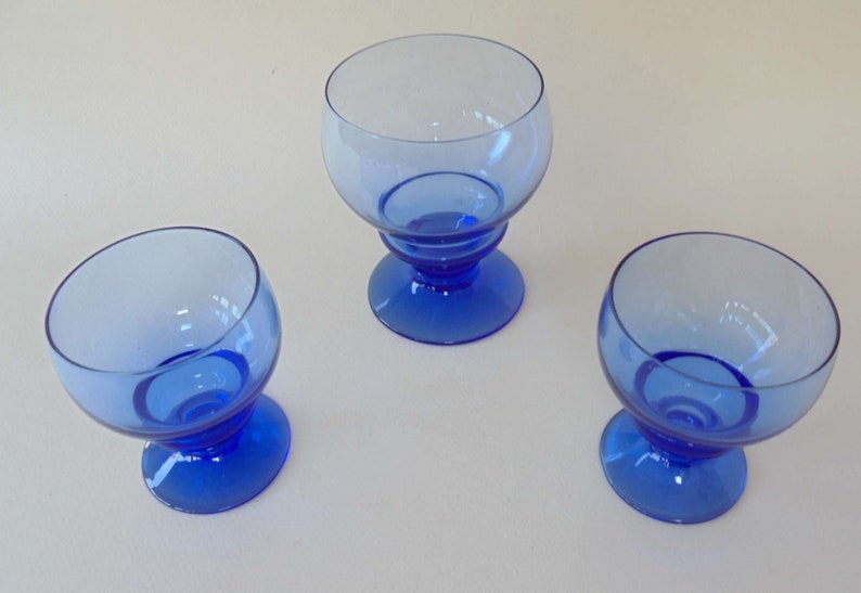 Op de afbeelding: Drie blauwe glazen bekers met een ronde kom en een korte steel. De bekers zijn gemaakt van helder glas met een blauwe tint.