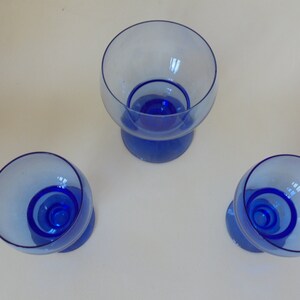 Op de afbeelding: Drie blauwe glazen dessertschaaltjes met een transparant glazen bovendeel en een blauwe glazen onderkant. De schaaltjes zijn in een driehoekige vorm op een wit oppervlak gerangschikt.