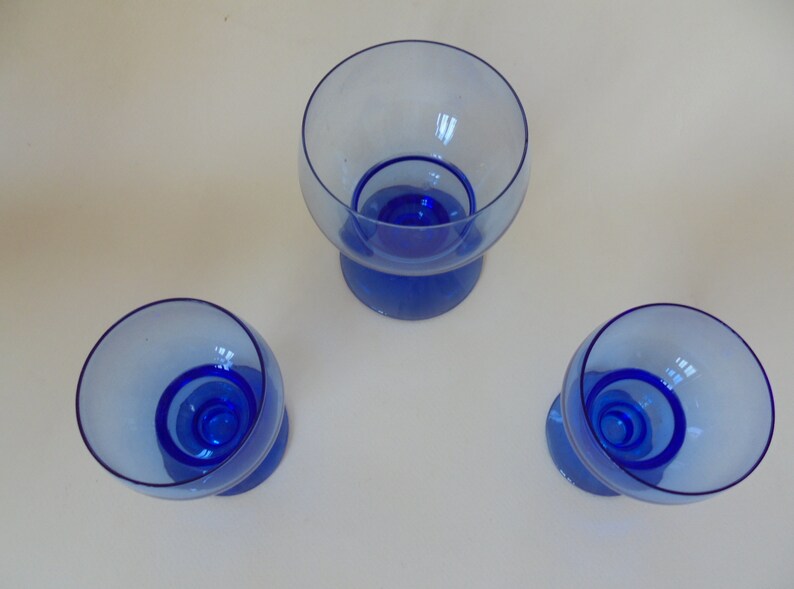Op de afbeelding: Drie blauwe glazen dessertschaaltjes met een transparant glazen bovendeel en een blauwe glazen onderkant. De schaaltjes zijn in een driehoekige vorm op een wit oppervlak gerangschikt.