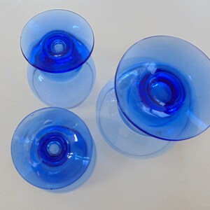 Op de afbeelding: Drie blauwe glazen kaarshouders met een brede basis en een smalle bovenkant. De kaarshouders zijn gemaakt van helder glas met een blauwe tint.