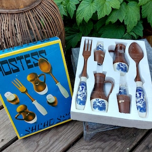 Peut inclure: Une boîte de set de salade Hostess avec un fond bleu et du texte blanc. La boîte contient un ensemble de serveurs de salade, des salières et poivrières et un ouvre-bouteille. L'ensemble est décoré d'un motif floral bleu et blanc.