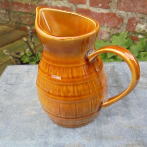 May include: A brown ceramic pitcher with a barrel design. The pitcher has a handle and a wide mouth.