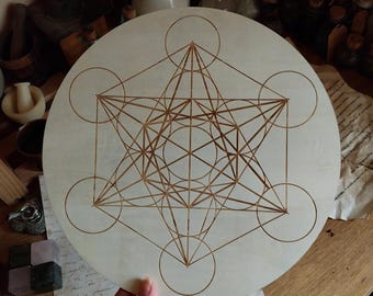 May include: A circular light-colored wooden plaque featuring a laser-engraved Metatron's Cube geometric pattern. The design consists of thin brown lines forming interconnected circles and straight lines, centered on the smooth, flat wooden surface.