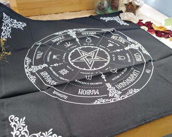 May include: A black altar cloth with a white pentagram and a circular design featuring astrological symbols and text. The cloth has decorative white corner accents and text including "MABON" and "OSTARA".