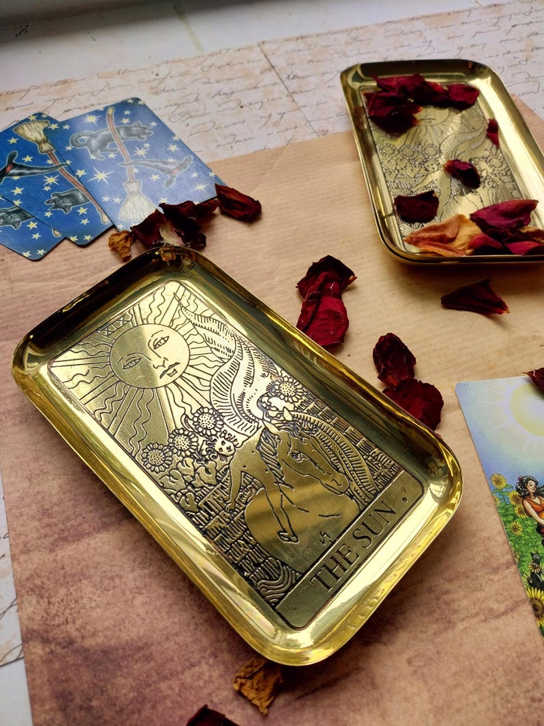 Pu&ograve; includere: Vassoio rettangolare color oro con un'immagine incisa del sole e le parole "THE SUN". Il vassoio &egrave; circondato da petali di rosa secchi e carte dei tarocchi. Il vassoio viene probabilmente utilizzato per scopi decorativi o spirituali.