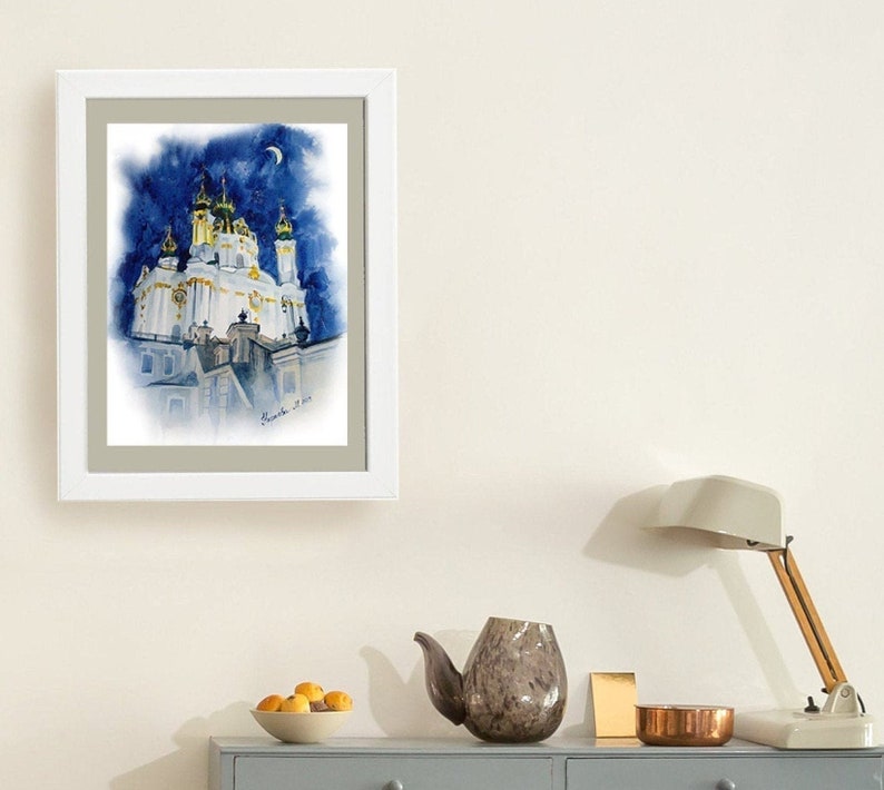 May include: Watercolor painting of a white church with gold accents against a blue night sky with a crescent moon. The church has multiple towers and domes. The painting is framed in a white frame.