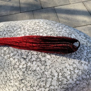 May include: Red and black ombre synthetic dreadlocks with a black rubber band.