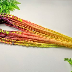 May include: A set of synthetic dreadlocks with a gradient of colors from purple to yellow. The dreadlocks are made of kanekalon hair and are approximately 24 inches long.