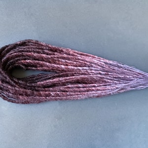 May include: A set of synthetic dreadlocks with a dark brown to light purple ombre color effect.