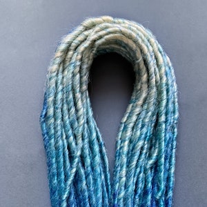 May include: A bundle of synthetic dreadlocks in shades of blue and white. The dreadlocks are twisted and have a ombre effect, transitioning from white to blue.