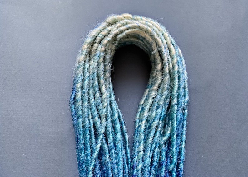 May include: A bundle of synthetic dreadlocks in shades of blue and white. The dreadlocks are twisted and have a ombre effect, transitioning from white to blue.