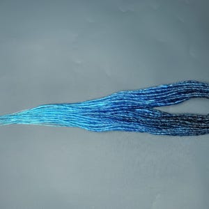 Puede incluir: Una larga hebra de rastas sintéticas azules degradado. Las rastas son de color azul claro en la parte superior y se desvanecen a un azul oscuro en la parte inferior.