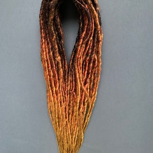 May include: A set of synthetic dreadlocks in black, brown, and orange shades. The dreadlocks are arranged in a loose bundle.