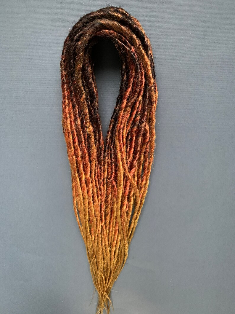 May include: A set of synthetic dreadlocks in black, brown, and orange shades. The dreadlocks are arranged in a loose bundle.