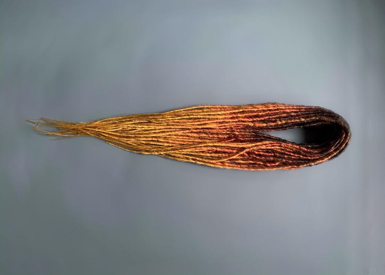 May include: A set of ombre synthetic dreadlocks in shades of brown, orange, and yellow. The dreadlocks are arranged in a loose circle.
