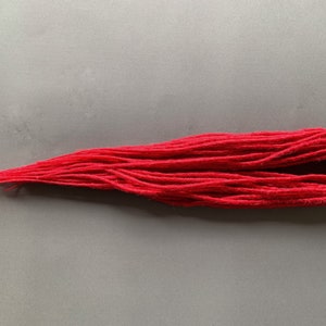 May include: A vibrant red yarn bundle, tightly wound and arranged on a gray surface. The yarn appears soft and textured, with a slightly frayed end. This craft supply is ideal for knitting, crocheting, or other fiber arts projects.