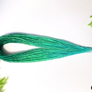 Könnte beinhalten: Ein Bündel synthetischer Dreadlocks in Ombre-Optik in Grün und Blau. Die Dreadlocks sind in einem lockeren Kreis angeordnet.