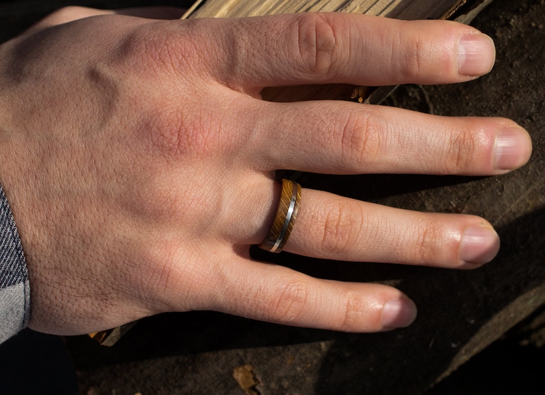 A ring crafted from brown oak wood featuring a smooth, polished silver inlay that runs horizontally around the center of the band. The wood grain is visible, showing a natural texture and deep brown tones throughout the ring.