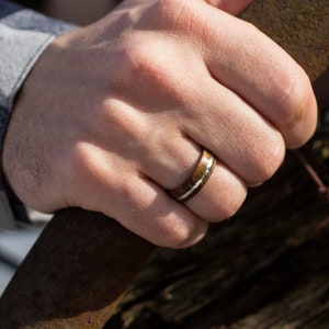 A ring featuring a dark brown oak wood grain band with a thin, polished silver inlay running horizontally through the center. The band has a smooth, rounded exterior surface and a consistent width around the entire circumference.