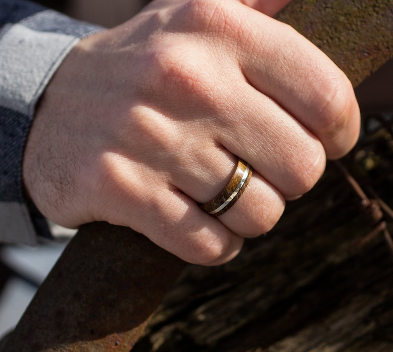 A ring featuring a dark brown oak wood grain band with a thin, polished silver inlay running horizontally through the center. The band has a smooth, rounded exterior surface and a consistent width around the entire circumference.