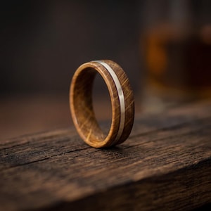 A ring featuring a band crafted from brown oak wood with a visible grain pattern, bisected by a thin, smooth, polished silver inlay that runs horizontally around the entire circumference of the circular band.
