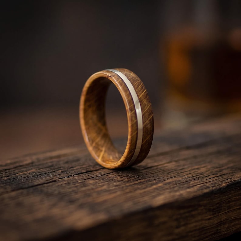 A ring featuring a band crafted from brown oak wood with a visible grain pattern, bisected by a thin, smooth, polished silver inlay that runs horizontally around the entire circumference of the circular band.