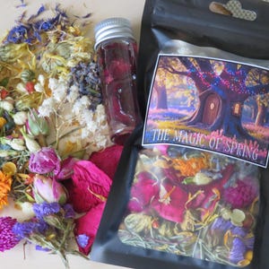 May include: An assortment of dried flowers and petals in various colors, including pink, purple, yellow, and white. A small glass bottle with a silver lid contains a red liquid. A black bag with a label that reads "THE MAGIC OF SPRING" is also present.