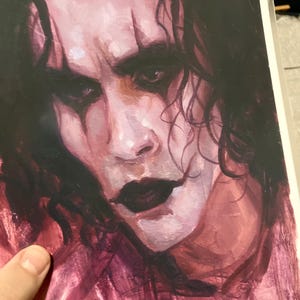 May include: A close-up painting of a man's face with dark hair and a dark, dramatic makeup look. The painting is done in a painterly style with visible brushstrokes. The artist's signature, "Anselena", is visible in the bottom right corner.