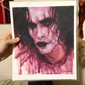 May include: A close-up painting of a man's face with dark hair and dark eyes. The painting is done in shades of pink and purple. The man's face is painted with dark makeup around the eyes and mouth. The artist's signature is in the bottom right corner of the painting.