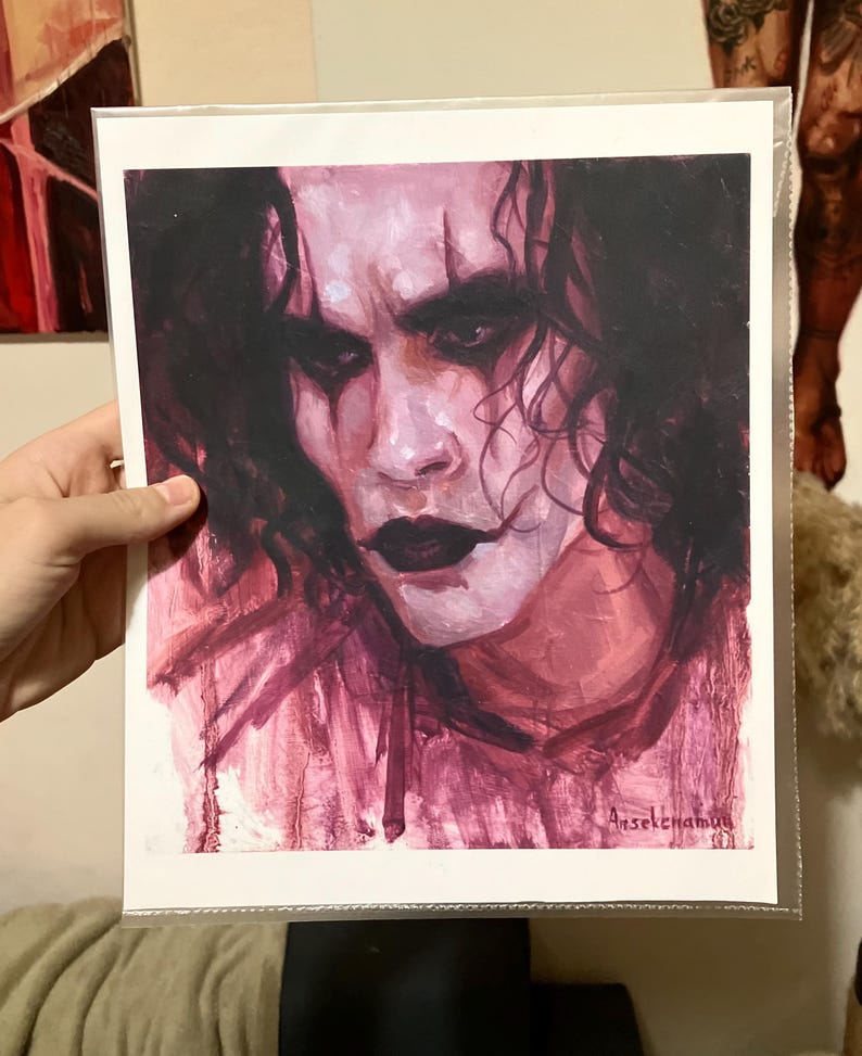 May include: A close-up painting of a man's face with dark hair and dark eyes. The painting is done in shades of pink and purple. The man's face is painted with dark makeup around the eyes and mouth. The artist's signature is in the bottom right corner of the painting.
