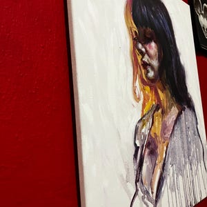 May include: An oil painting on canvas shows a woman with dark hair and a melancholic expression. The artwork uses white, purple, yellow, and black, with visible brushstrokes and paint drips. The canvas is mounted on a wooden frame.