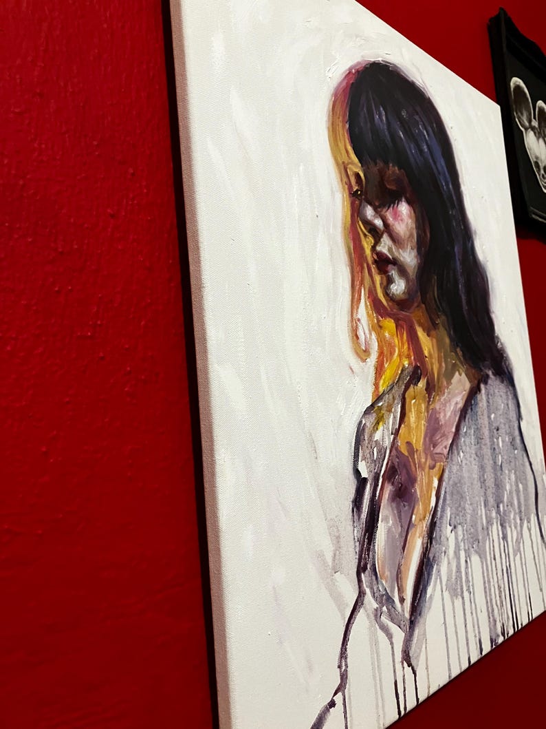 May include: An oil painting on canvas shows a woman with dark hair and a melancholic expression. The artwork uses white, purple, yellow, and black, with visible brushstrokes and paint drips. The canvas is mounted on a wooden frame.