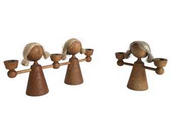 Puede incluir: Tres candelabros de madera con forma de personas con los brazos extendidos sosteniendo velas. Los candelabros están hechos de madera natural y tienen un acabado rústico.