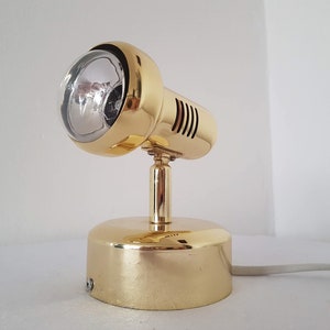 Puede incluir: Un foco ajustable de color dorado con una pantalla redonda de vidrio transparente. El foco tiene una base redonda y un cable.