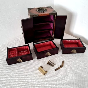 May include: A wooden jewelry box with a red velvet interior and brass accents. The box has three drawers and a hinged lid. The box is open and the drawers are pulled out.