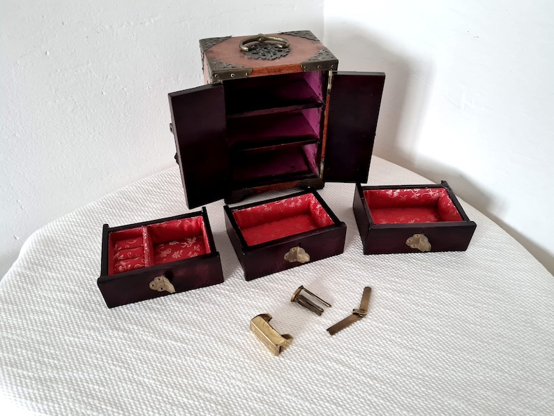 May include: A wooden jewelry box with a red velvet interior and brass accents. The box has three drawers and a hinged lid. The box is open and the drawers are pulled out.