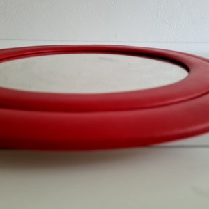 May include: A round mirror with a red frame. The frame has two layers, creating a double-ring effect.