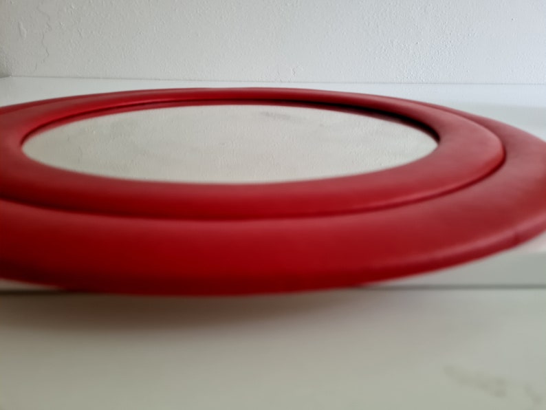 May include: A round mirror with a red frame. The frame has two layers, creating a double-ring effect.
