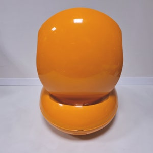 May include: A bright orange, egg-shaped chair with a smooth, glossy finish. The chair is designed with a rounded, curved back and a wide, circular base.