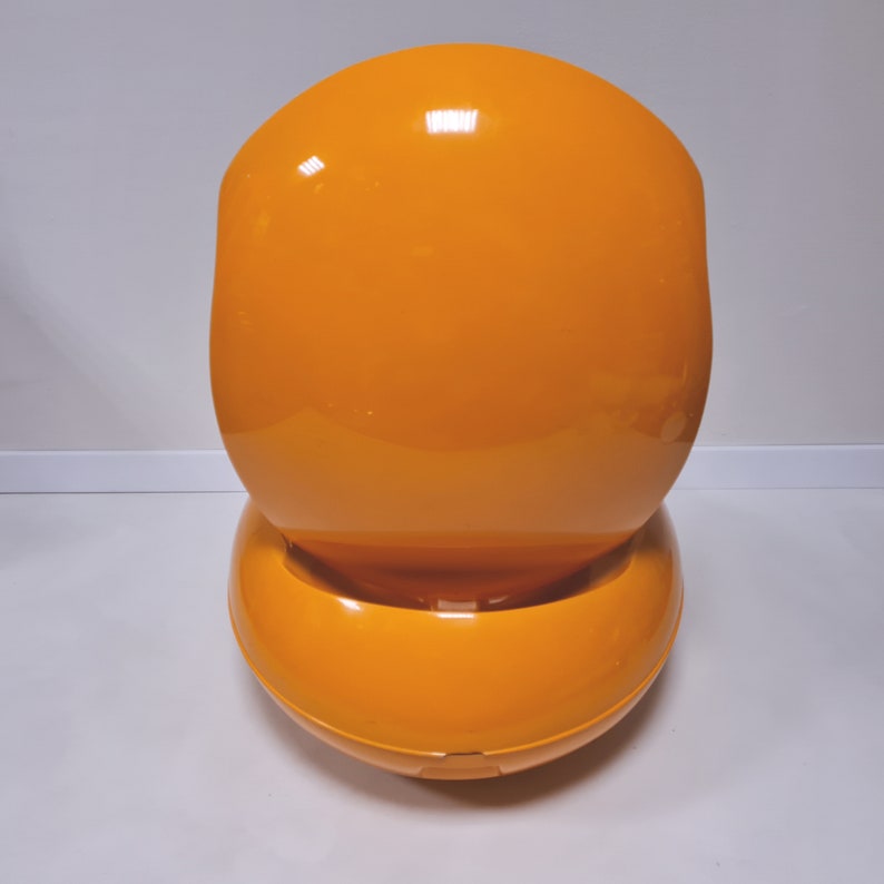 May include: A bright orange, egg-shaped chair with a smooth, glossy finish. The chair is designed with a rounded, curved back and a wide, circular base.