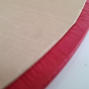 May include: Close-up of a beige fabric with a red leather trim. The fabric has a subtle texture and the leather trim is slightly frayed.