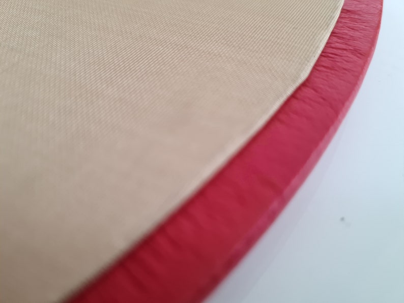 May include: Close-up of a beige fabric with a red leather trim. The fabric has a subtle texture and the leather trim is slightly frayed.