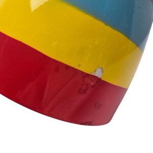 May include: Close-up of a cylindrical object with a vibrant, painted design. The object features horizontal bands of red, yellow, and blue. The paint shows signs of wear, with some areas chipped or faded.