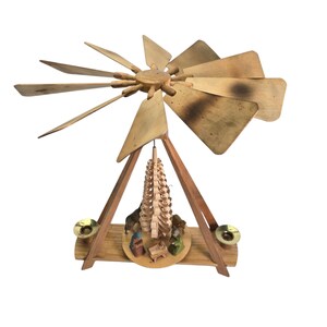 May include: A wooden Christmas pyramid with a rotating propeller and a nativity scene at the base. The pyramid is decorated with a wooden tree and a small stable with figures of Mary, Joseph, and the baby Jesus.
