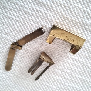 May include: Three pieces of a brass lock, including a rectangular lock plate, a hinged latch, and a keyhole cover.