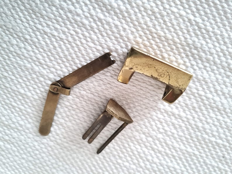 May include: Three pieces of a brass lock, including a rectangular lock plate, a hinged latch, and a keyhole cover.