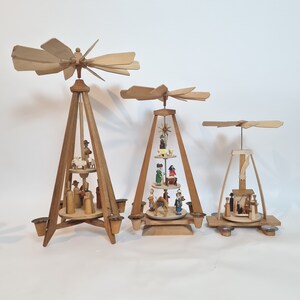 May include: Three wooden Christmas pyramids with intricate carvings and painted figures. The largest pyramid features a star at the top and a nativity scene with a camel, shepherds, and angels. The middle pyramid has a star at the top and a nativity scene with a camel, shepherds, and angels. The smallest pyramid has a star at the top and a nativity scene with a camel, shepherds, and angels.