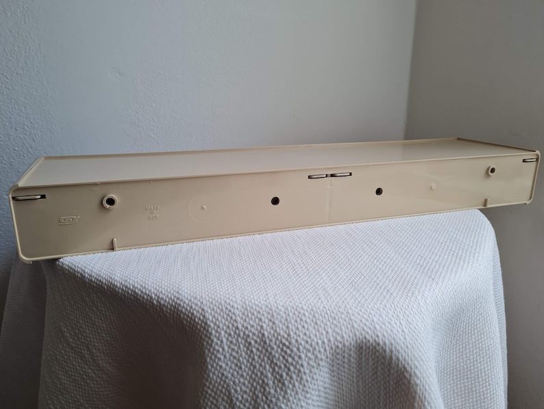 Puede incluir: Una estanter&iacute;a de pl&aacute;stico beige con dos peque&ntilde;os agujeros en la parte superior y dos agujeros m&aacute;s grandes en la parte inferior. La estanter&iacute;a tiene una etiqueta que dice "Hecho en China".
