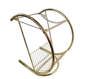 May include: A gold metal side table with a glass top and a wire magazine rack. The table has a curved design and a circular base.